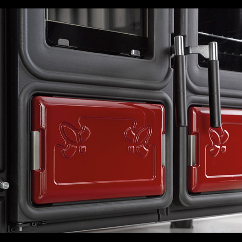 Détail des portes émaillées rouges de la cuisinière à bois Milly avec poignées chromées