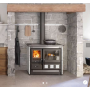 Cuisinière à bois Rosa XXL Petra 11 kW élégante dans une cuisine en pierre, avec bûches et accessoires de cuisson.