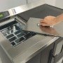 Une main soulève le couvercle en acier inoxydable de la cuisinière à granulés encastrable, vue du dessus.